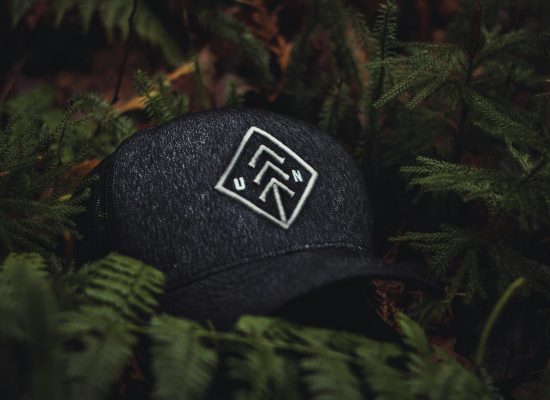 Close-up of a dark baseball cap with an embroidered design nestled among green ferns, creating a nature-themed concept.